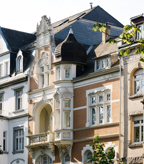 Historisches Gebäude mit aufwendig verzierter Fassade, Erker, Rundbogenfenstern und Schieferdach.