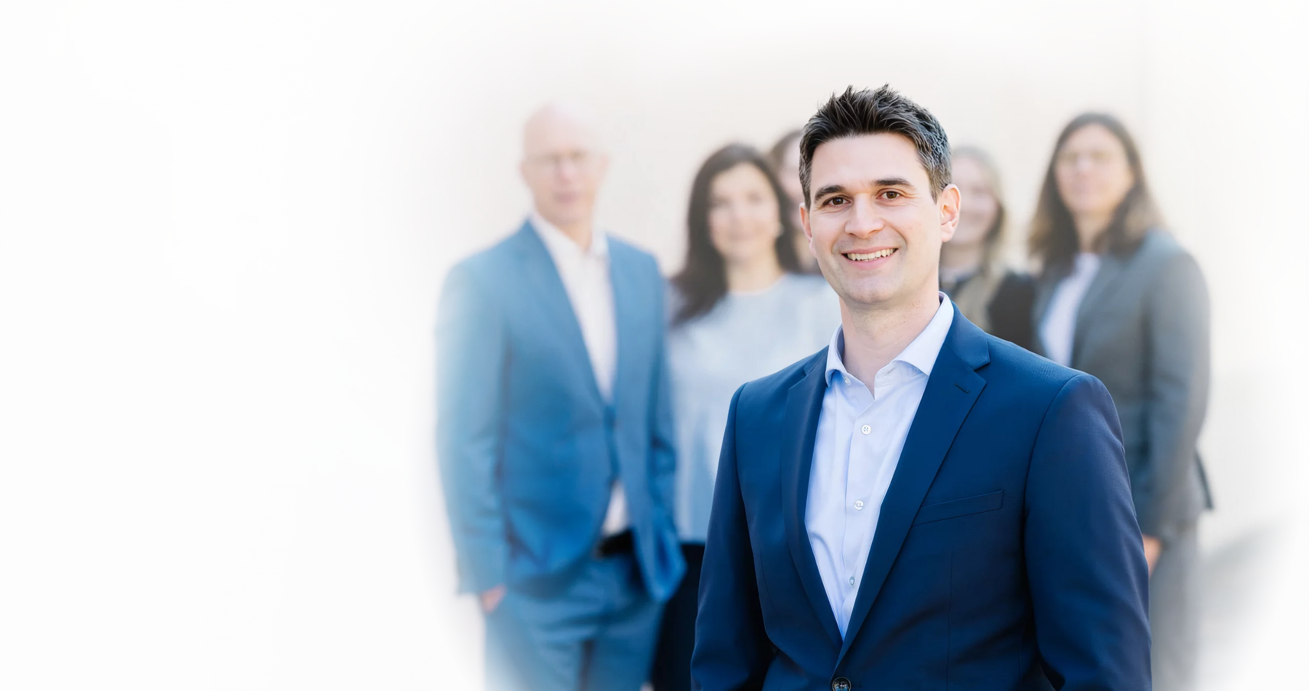 Lächelnder Mitarbeiter von Dr. Widdau & Partner im Vordergrund, dahinter weitere Mitglieder des Teams.