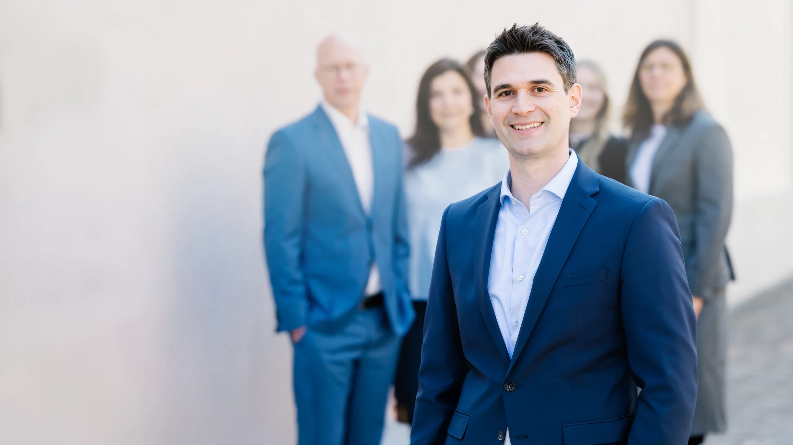 Lächelnder Mitarbeiter von Dr. Widdau & Partner im Vordergrund, dahinter weitere Mitglieder des Teams.