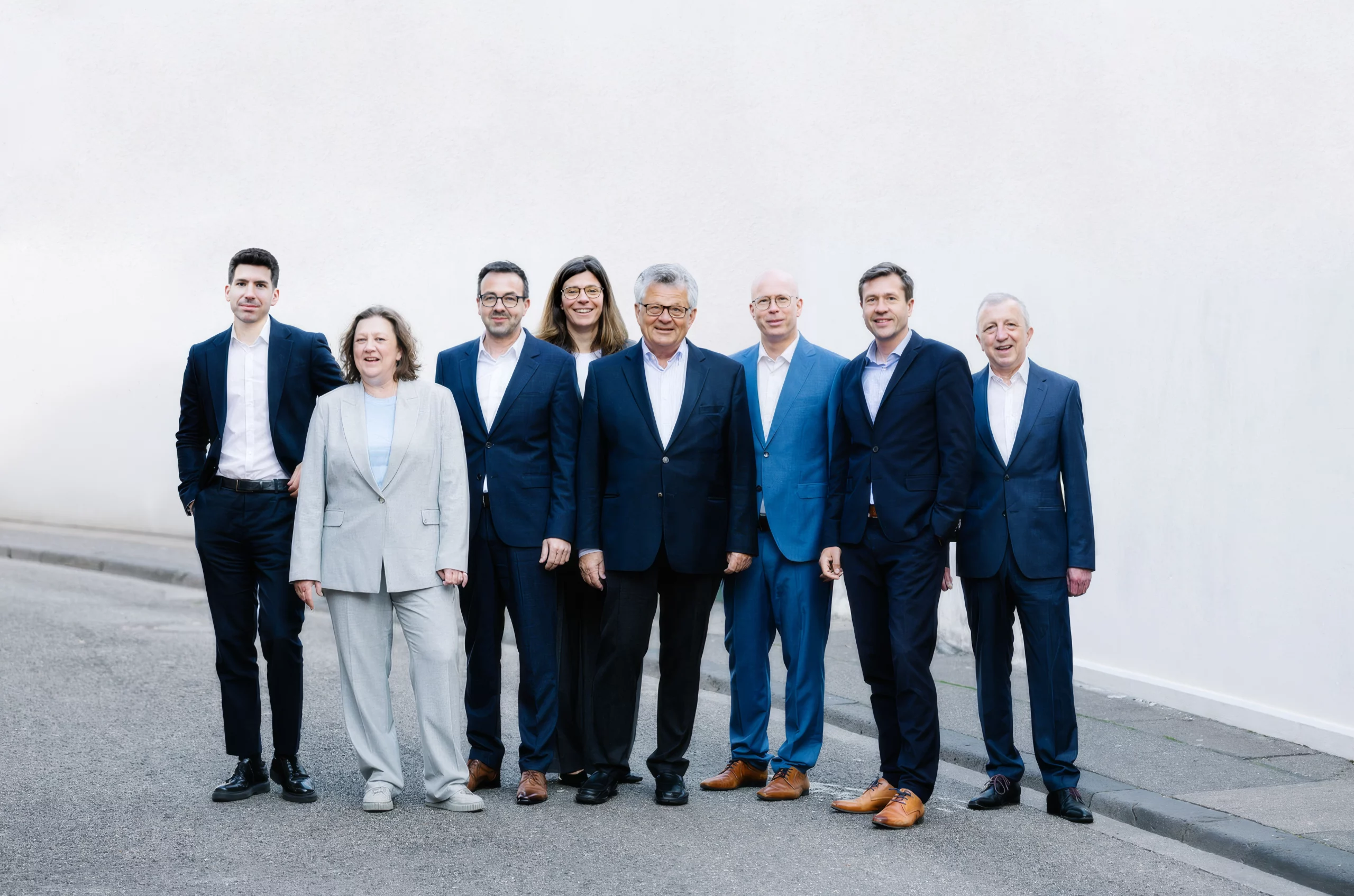 Acht Partner von Dr. Widdau & Partner stehen gemeinsam vor einer hellen Gebäudewand.