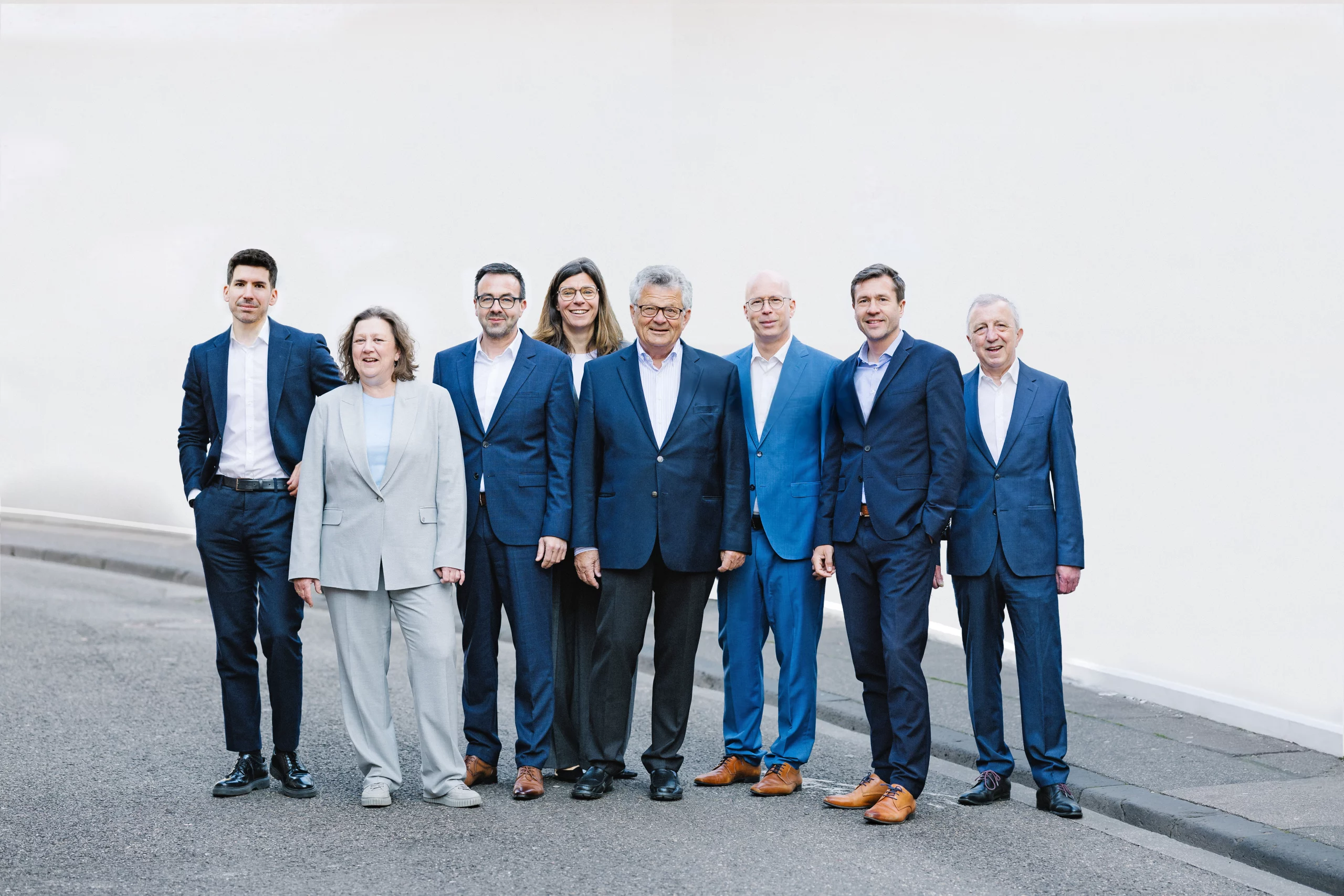 Acht Partner von Dr. Widdau & Partner stehen gemeinsam vor einer weißen Wand.