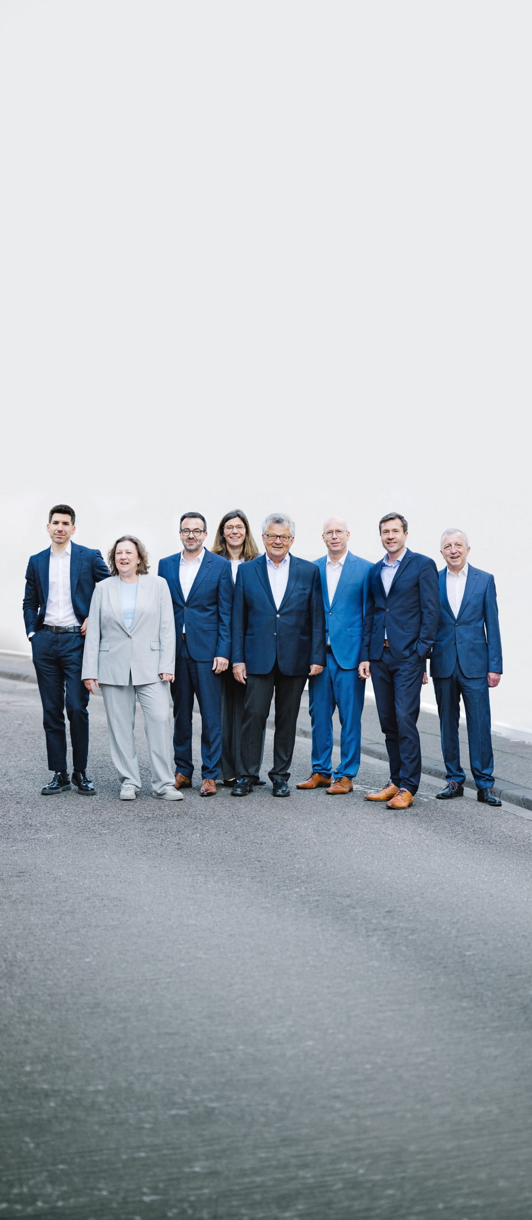 Acht Partner von Dr. Widdau & Partner stehen gemeinsam vor einer weißen Wand.
